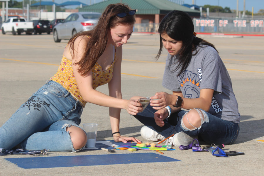 Seniors Bri Johnston and Sofia Davis search up what they want to paint on Johnstons spot. Many students painted their nicknames and a small symbol that represented themselves on their spot.
